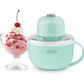 A mint green countertop ice cream maker shown next to a glass bowl of pink strawberry ice cream topped with whipped cream and a cherry, on a white background.