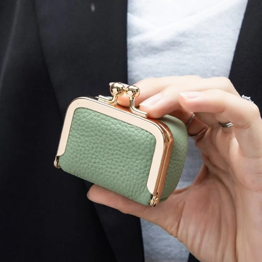 Hand holding a small green purse with gold clasp against a blurred background