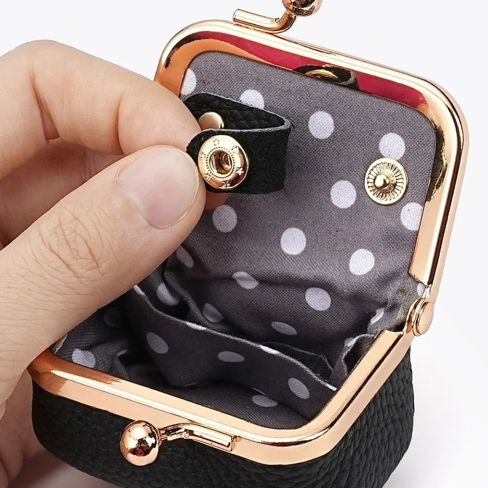 Small black purse with gold accents and a polka dot interior held by a hand.