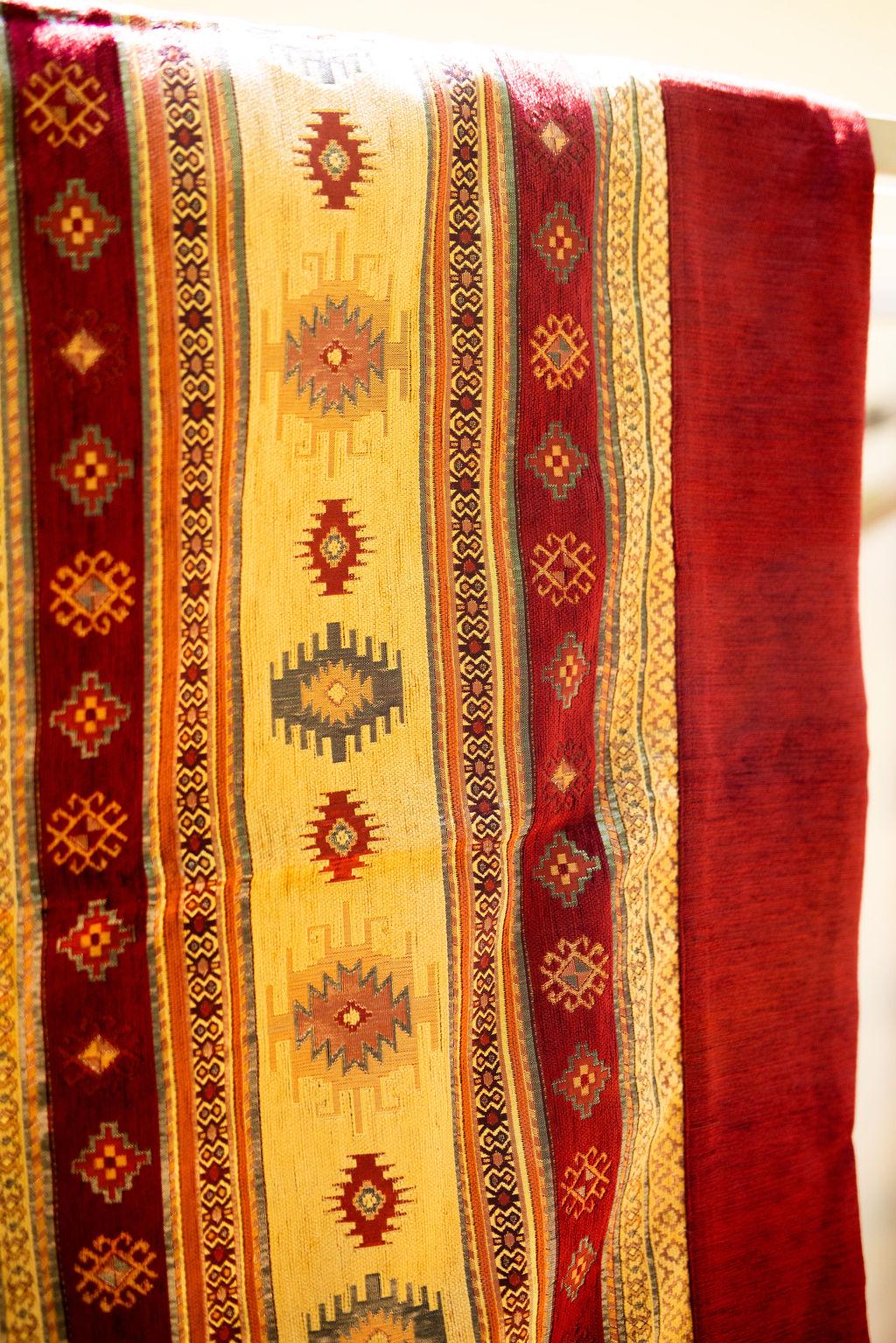 Corner detail of burgundy Turkish rug with yellow geometric bands and a pale tassel