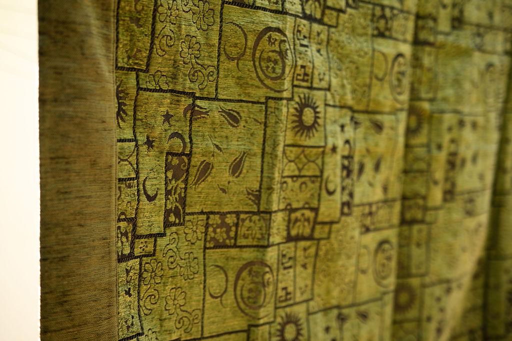 Angled detail of olive rug showing dark framed botanical motifs and wide border