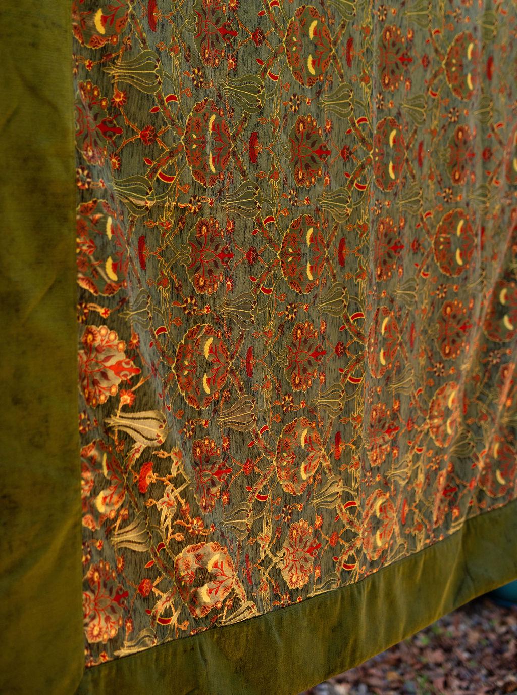 Close-up of red and rust floral motifs on a muted green Turkish rug