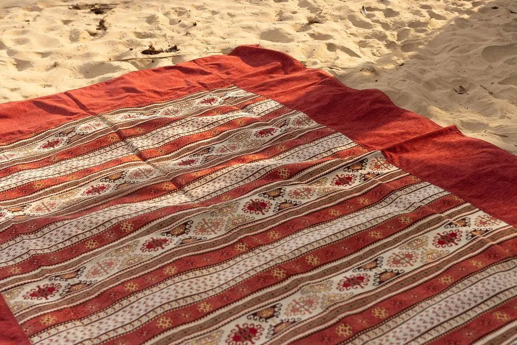 Red and cream Turkish striped rug displayed on sand showing the patterned center