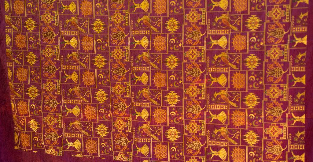 Burgundy rug edge with gold-tone motifs and orange tassel detail