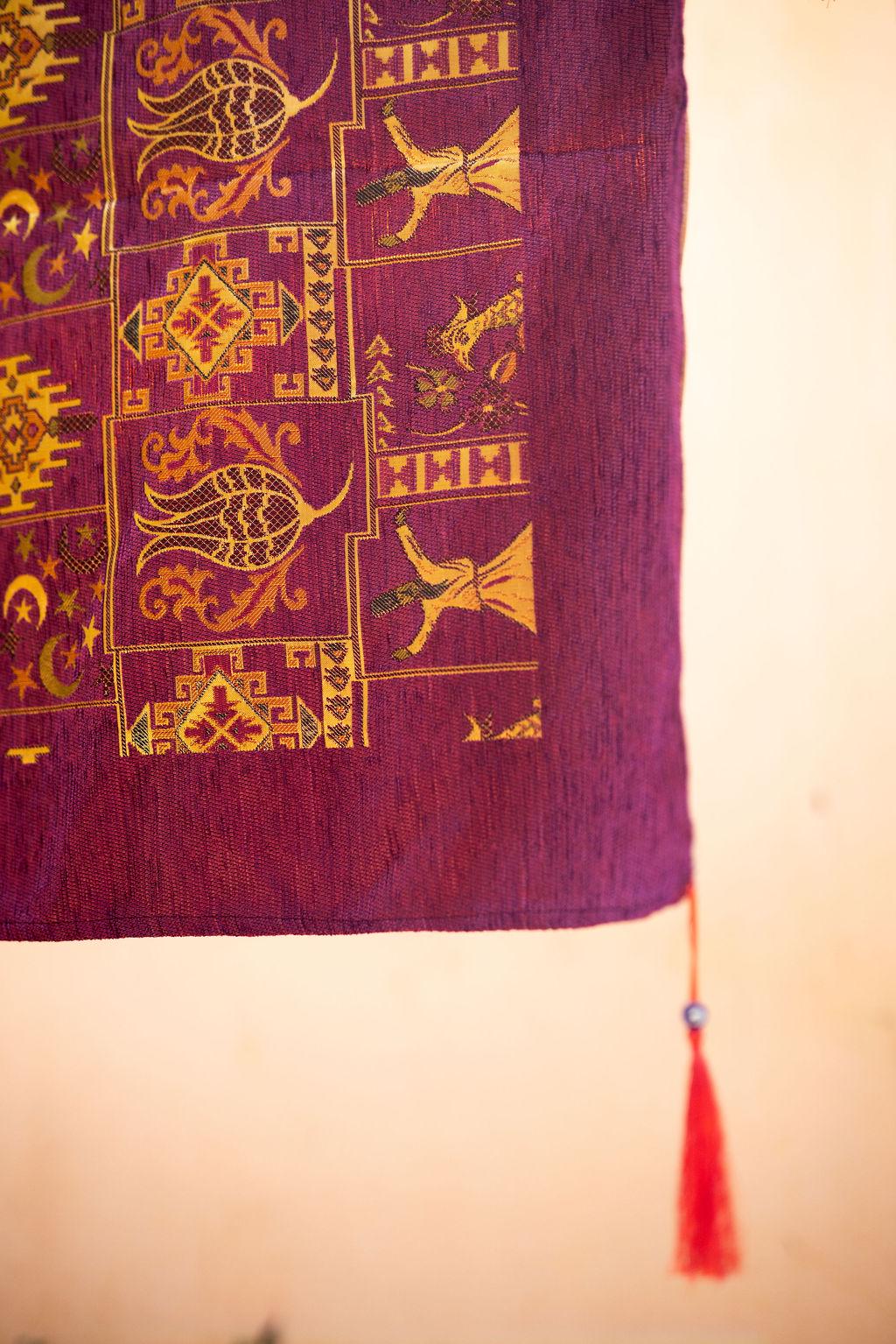Angled close-up of burgundy rug with gold-tone flowers, birds, crescents and stars